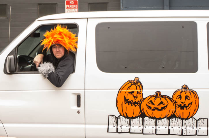 man with orange wig in white van with Halloween pumpkins on the side.