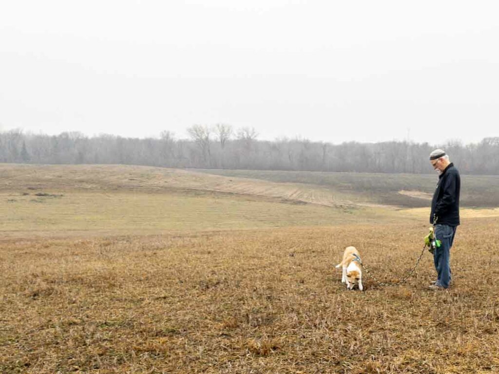 Man and small dog standing in a field.